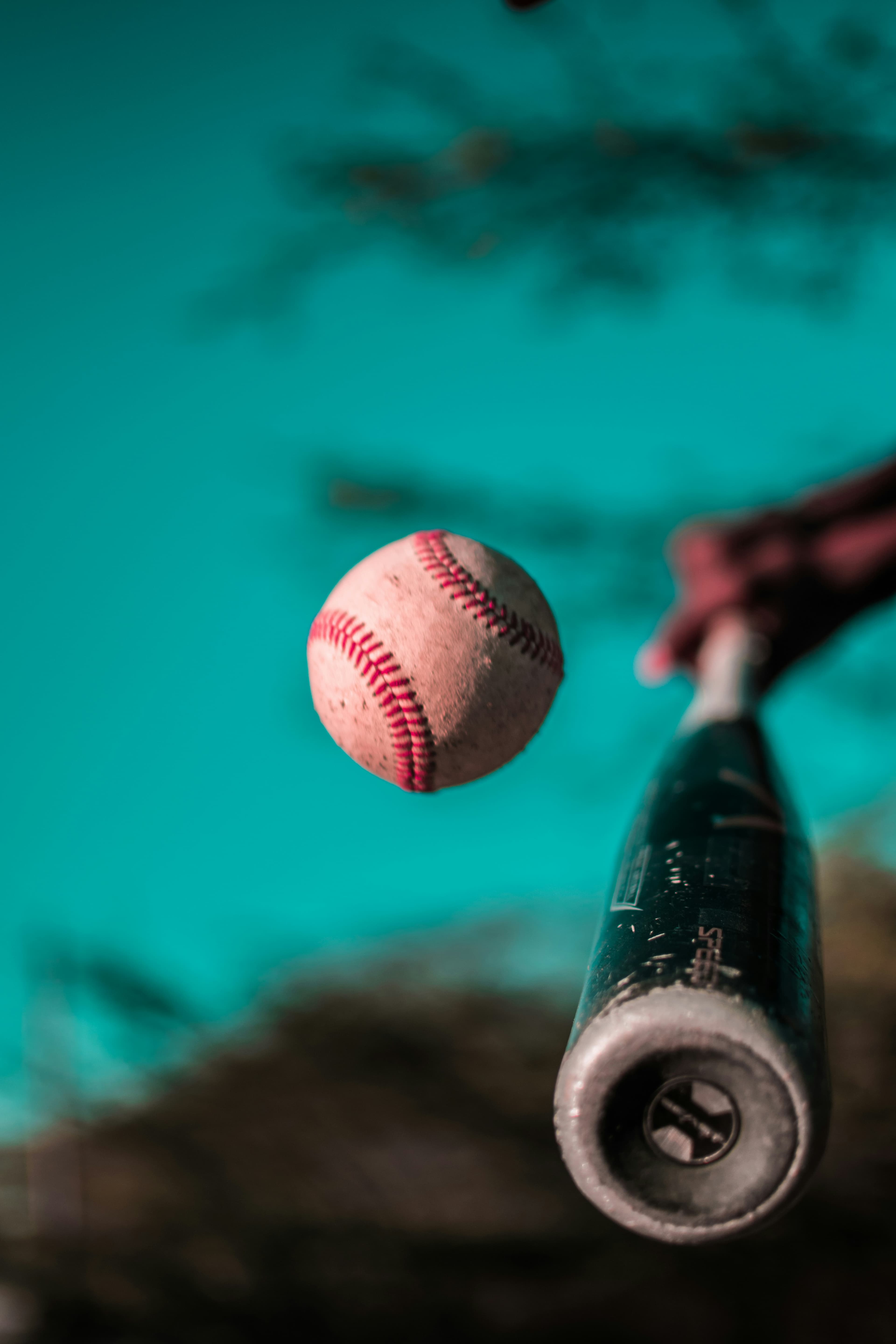 Bat connecting with a baseball under a teal sky