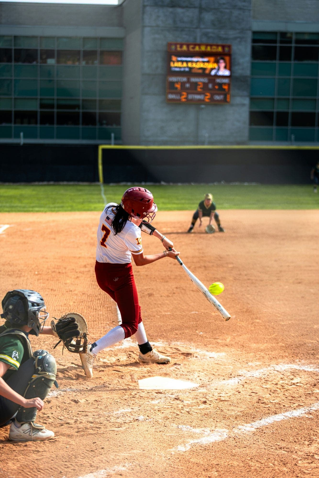 Fastpitch hitter making contact at the plate with the catcher set behind her
