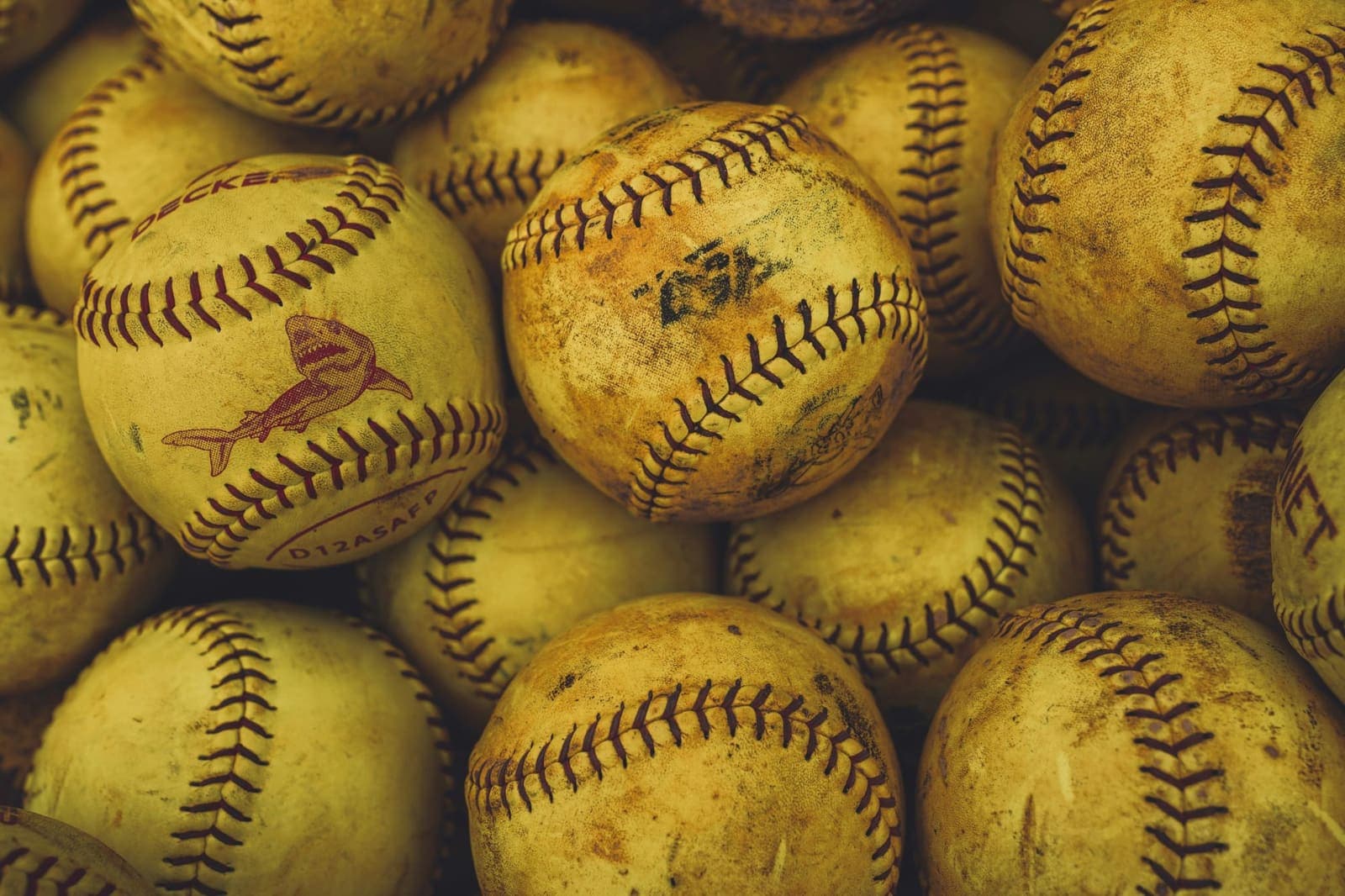 A bucket's worth of worn yellow softballs with red stitching, piled together